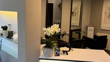 Empfangsbereich eines Salons mit modernem Design, stilvoller Beleuchtung und Markenlogo auf dem Tresen.