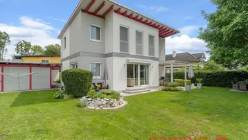Modernes Einfamilienhaus mit gepflegtem Garten, Terrasse und Carport unter blauem Himmel.