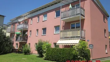 Mehrfamilienhaus mit rosafarbener Fassade, Balkonen und gepflegtem Vorgarten.