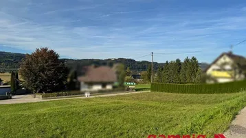 Weitläufige Grünfläche mit Blick auf die umliegende Landschaft und Berge unter blauem Himmel.