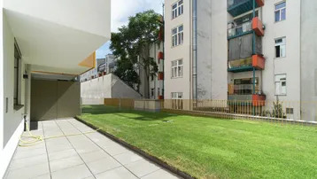 Gepflasterte Terrasse neben einer Rasenfläche mit Blick auf umliegende Gebäude und viel Grün.