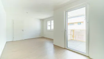 Helles, leeres Zimmer mit hellem Parkettboden und Zugang zu einem Balkon.
