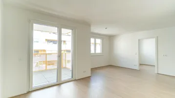 Helles, leeres Wohnzimmer mit Parkettboden und Zugang zu einem Balkon, bereit zur individuellen Gestaltung.