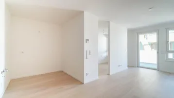 Heller, leerer Raum mit hellem Holzfußboden und Zugang zu einem Balkon oder einer Terrasse.