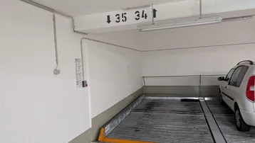 Helle Tiefgarage mit modernem Doppelparker-System für zwei Fahrzeuge und klarer Beschilderung.