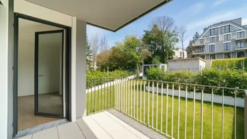 Heller Balkon mit Fliesenboden und Blick ins Grüne sowie auf umliegende Gebäude.