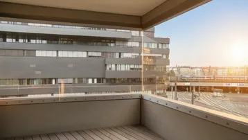 Balkon mit Holzboden und Glasbrüstung, bietet einen weiten Blick auf die Stadt und umliegende Gebäude.