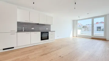 Helle, offene Küche mit weißen Schränken, Holzboden und Zugang zu großen Fenstern.