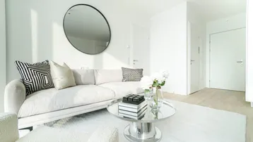 Helles Wohnzimmer mit modernem Sofa, Couchtisch und rundem Spiegel an der weißen Wand.