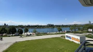 Panoramablick vom Balkon auf die Donau und die Stadtlandschaft unter blauem Himmel.