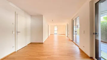 Helles, leeres Wohnzimmer mit Parkettboden und Zugang zur Terrasse.