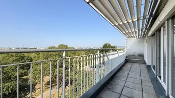 Geräumiger Balkon mit Fliesenboden, Metallgeländer und weitem Blick über die Stadt und viel Grün.