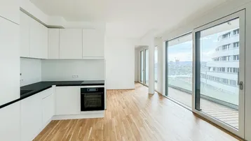 Heller offener Wohnbereich mit moderner Einbauküche, Parkettboden und Zugang zu einem Balkon.
