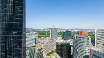 Panoramablick über die moderne Stadtlandschaft mit Hochhäusern, grünen Flächen und Bergen im Hintergrund.
