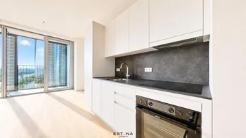 Moderne Küche mit weißen Schränken, dunkler Arbeitsplatte und Zugang zu einem Balkon mit Weitblick.
