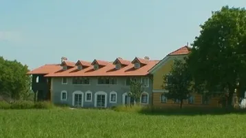 Großes Landhaus mit traditionellem Ziegeldach und grüner Umgebung, umgeben von weiten Feldern.
