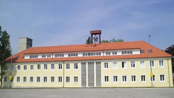 Ein großes, gelbes Gebäude mit einem markanten roten Ziegeldach und vielen Fenstern unter blauem Himmel.