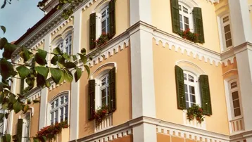 Historisches Gebäude mit gelber Fassade, grünen Fensterläden und Blumenkästen, gut gepflegt.