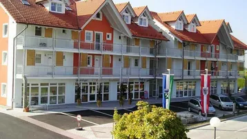 Mehrstöckiges Gebäude mit roten Ziegeldächern, zahlreichen Balkonen und einer hellen Fassade.