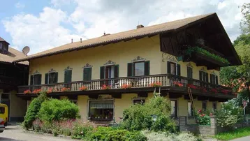 Traditionelles bayerisches Haus mit großem Holzbalkon, grünen Fensterläden und gepflegtem Vorgarten.