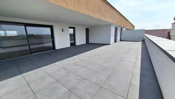 Geräumige Dachterrasse mit modernen Fliesen und weitem Blick in die Landschaft unter blauem Himmel.