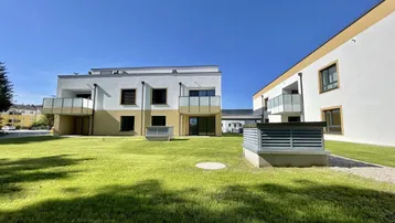 Moderne Wohngebäude mit weißer und gelber Fassade, umgeben von einer gepflegten Rasenfläche unter blauem Himmel.