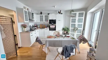 Helle, offene Küche mit weißen Schränken, Essbereich und Zugang zum Balkon.
