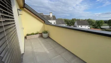 Geräumige Dachterrasse mit Fliesenboden und Blick auf die umliegenden Häuser und den Himmel.
