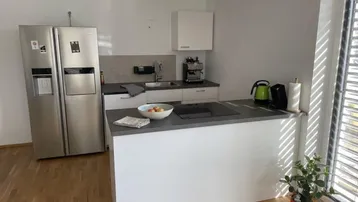 Moderne Küche mit weißen Schränken, Kücheninsel, großem Kühlschrank und Holzboden.