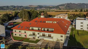 Luftaufnahme eines modernen Wohngebäudes mit rotem Ziegeldach und weitläufiger Grünfläche in ländlicher Umgebung.