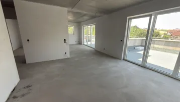 Geräumiger, unfertiger Innenraum mit Betonboden und großen Schiebetüren zur Terrasse.