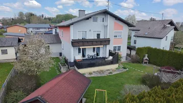 Blick auf das Haus mit großer Terrasse, gepflegtem Garten und Spielbereich.