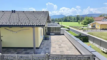 Weitläufige Terrasse mit Blick auf grüne Wiesen und die umliegende Berglandschaft unter blauem Himmel.