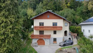 Traditionelles Haus mit Balkonen, umgeben von viel Grün und einem Spielbereich im Vorgarten.