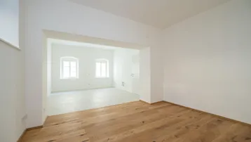 Helles, leeres Zimmer mit neuem Holzboden und offenem Durchgang zu einem weiteren Bereich.