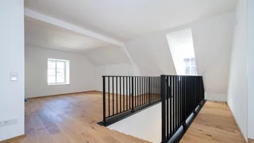 Offener Dachbodenbereich mit Holzboden, Dachschräge und schwarzem Metallgeländer, hell und geräumig.