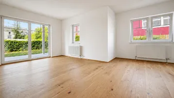 Helles, leeres Zimmer mit Holzboden, weißen Wänden und direktem Zugang zum Garten.