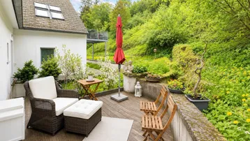 Gemütliche Holzterrasse mit Gartenmöbeln, Sonnenschirm und üppiger grüner Umgebung.