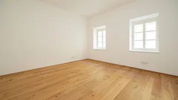 Helles, leeres Zimmer mit neuem Holzparkettboden und zwei Fenstern, bereit zur individuellen Gestaltung.