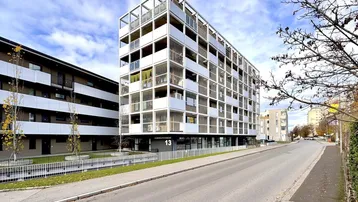 Modernes Mehrfamilienhaus mit vielen Balkonen und einer klaren, strukturierten Fassade an einer Straße.