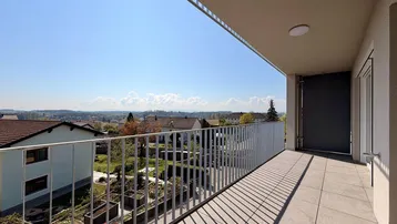 Geräumiger Balkon mit Fliesenboden und weitem Blick über die Landschaft und umliegende Häuser.