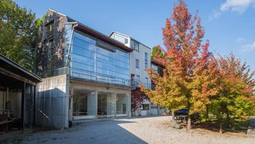 Modernes Gebäude mit Glasfassade und Holzelementen, umgeben von Herbstbäumen unter blauem Himmel.