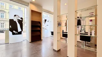 Heller Friseursalon mit großen Schaufenstern, modernen Glasregalen und Fliesenboden.