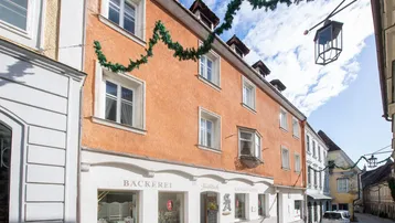 Historisches Gebäude mit orangefarbener Fassade und Geschäften im Erdgeschoss an einer Kopfsteinpflasterstraße.