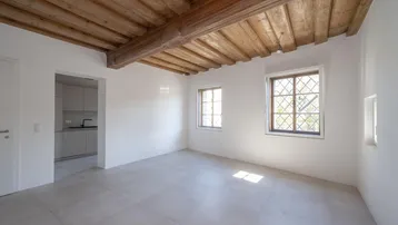 Heller Raum mit Holzbalkendecke, Fliesenboden und Blick ins Grüne durch Sprossenfenster.