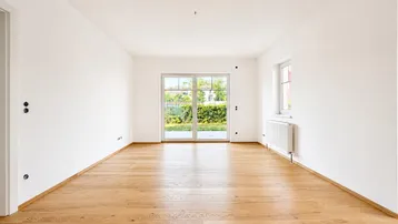 Helles Zimmer mit Holzboden, weißen Wänden und Zugang zu einem Gartenbereich.