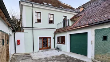 Historisches Gebäude mit hellgrüner Fassade, Holztüren und einem Garagentor in einem Innenhof.