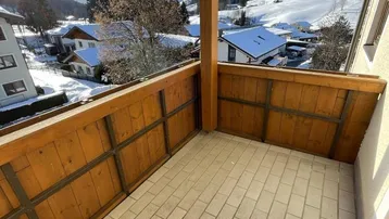 Sonniger Balkon mit Fliesenboden und Holzelementen, bietet einen weiten Blick auf die verschneite Berglandschaft.