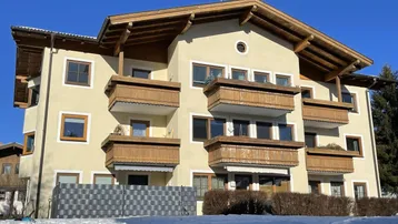 Mehrfamilienhaus mit traditioneller Holzverkleidung an den Balkonen und einem Satteldach in verschneiter Umgebung.