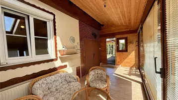Gemütlicher Wintergarten mit Rattanmöbeln, Fliesenboden und Holzdecke, ideal zum Entspannen.